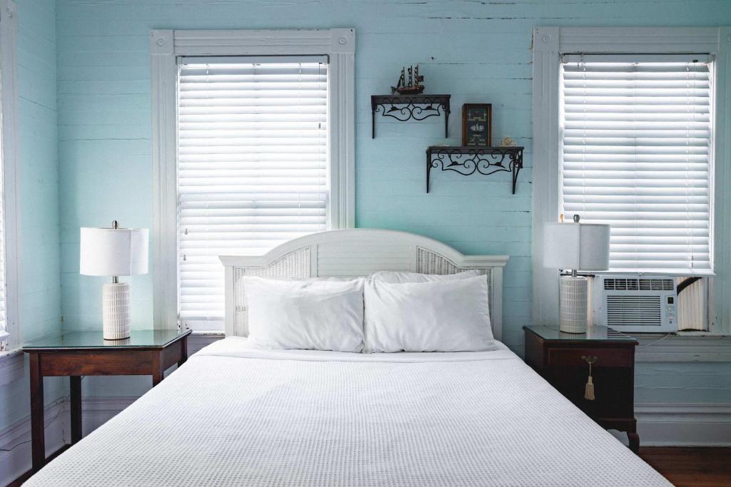 un lit blanc dans une chambre bleue avec deux fenêtres dans l'établissement Curry House - Room 1, à Key West