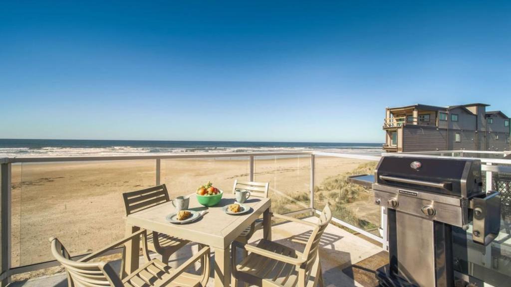 a table and chairs on a balcony with a grill and the beach at Moonlight by AvantStay Modern Home w Views Direct Access to Rockaway Beach in Rockaway Beach