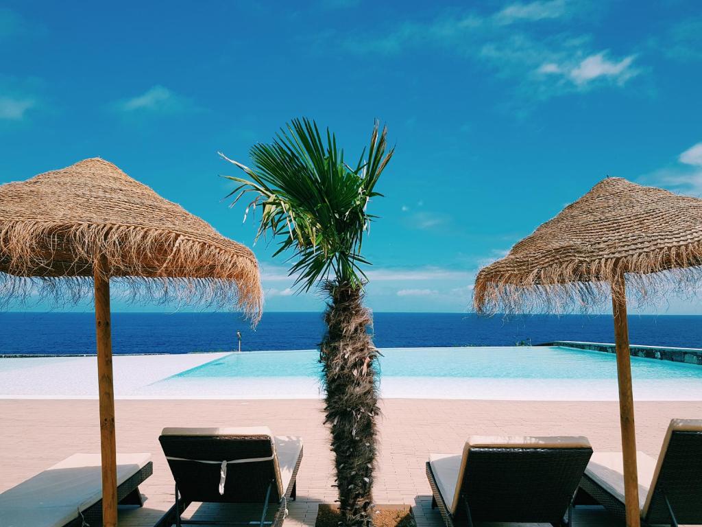 einen Strand mit Liegestühlen und Sonnenschirmen und einer Palme in der Unterkunft Pedras do Mar Resort & Spa in Fenais da Luz