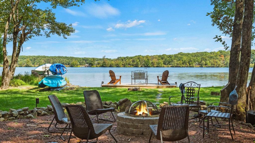 a group of chairs around a fire pit next to a lake at Lake Daze by AvantStay Lakefront w Modern Interior Enclosed Porch Hot Tub in Long Pond