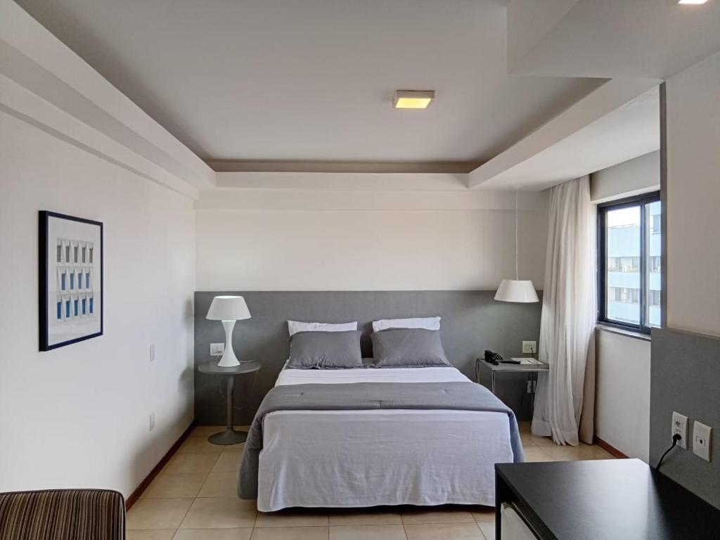 a white bedroom with a bed and a table at Suítes Executivas in Feira de Santana