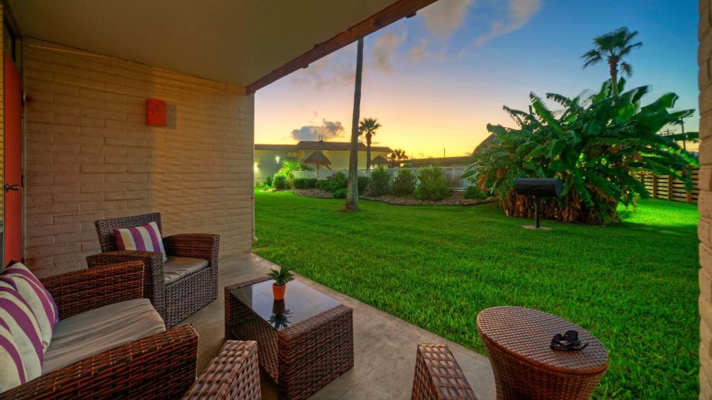 a patio with wicker chairs and a table and a lawn at Beach Boardwalk Access Pool Remodeled Interior Tropical Haven by AvantStay in Port Aransas