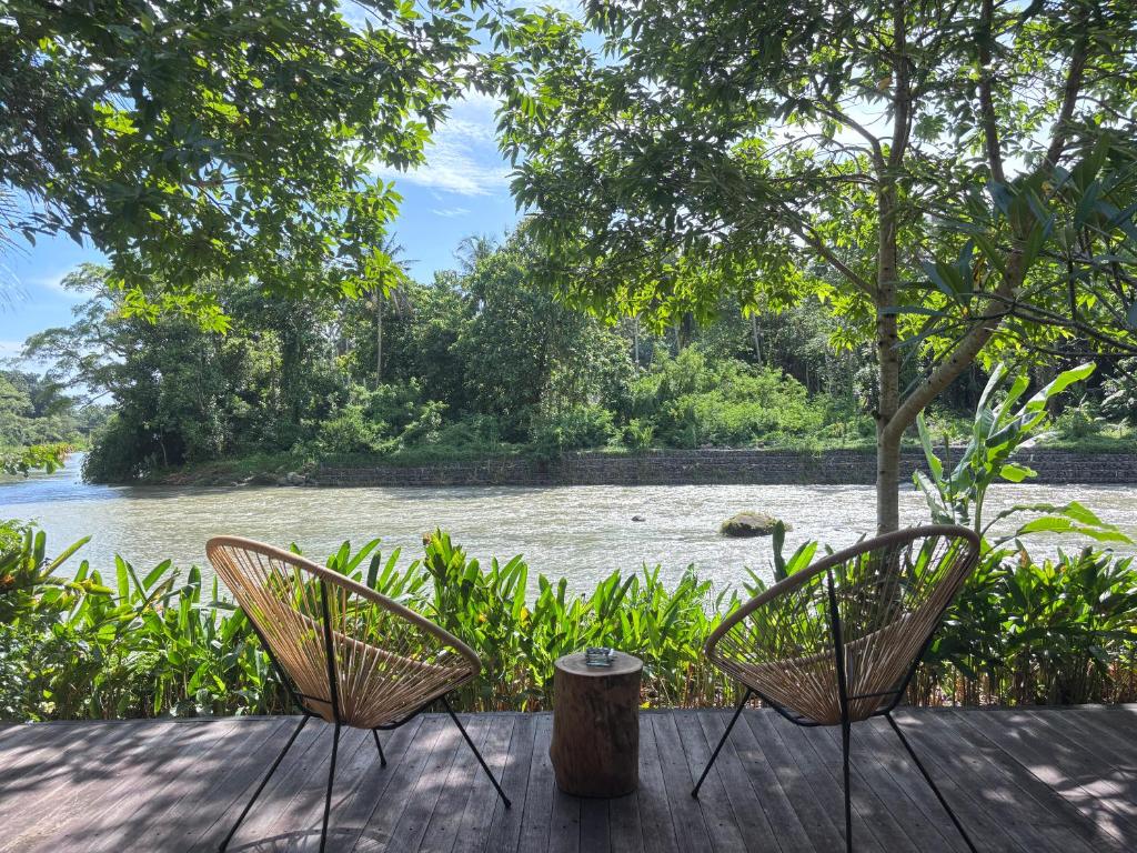 two chairs sitting on a deck overlooking a river at Balian River Hut in Balian