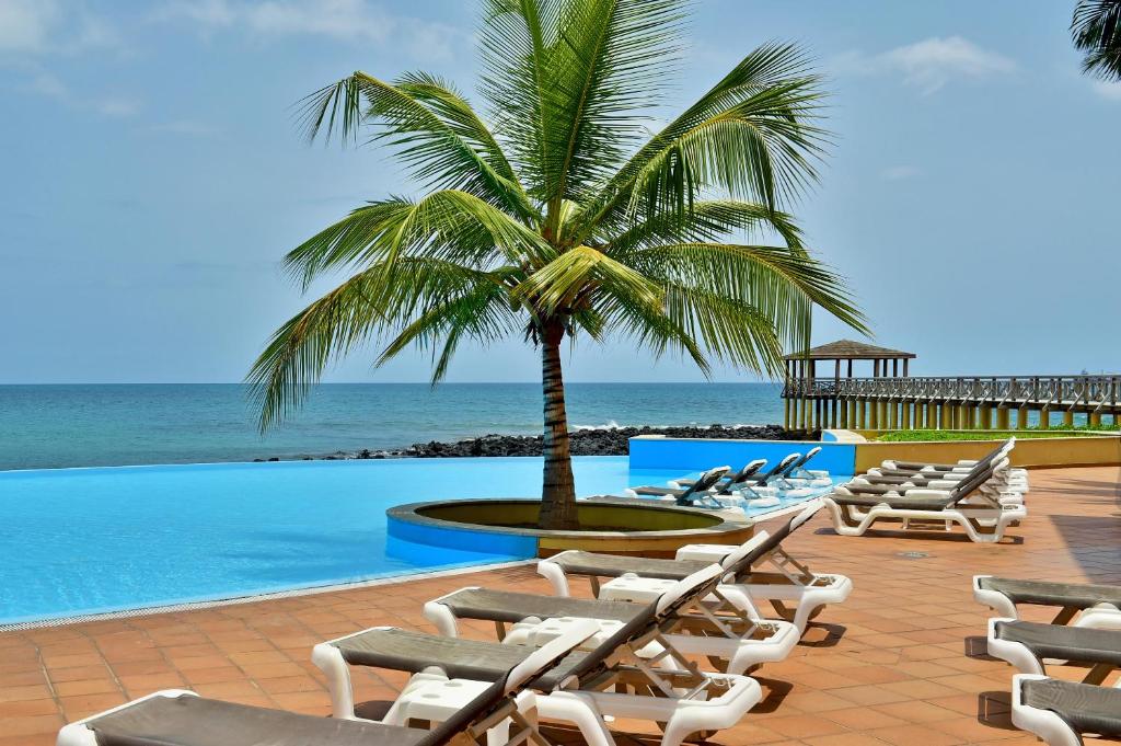 a row of lounge chairs and a palm tree next to a pool at Pestana Sao Tome in São Tomé