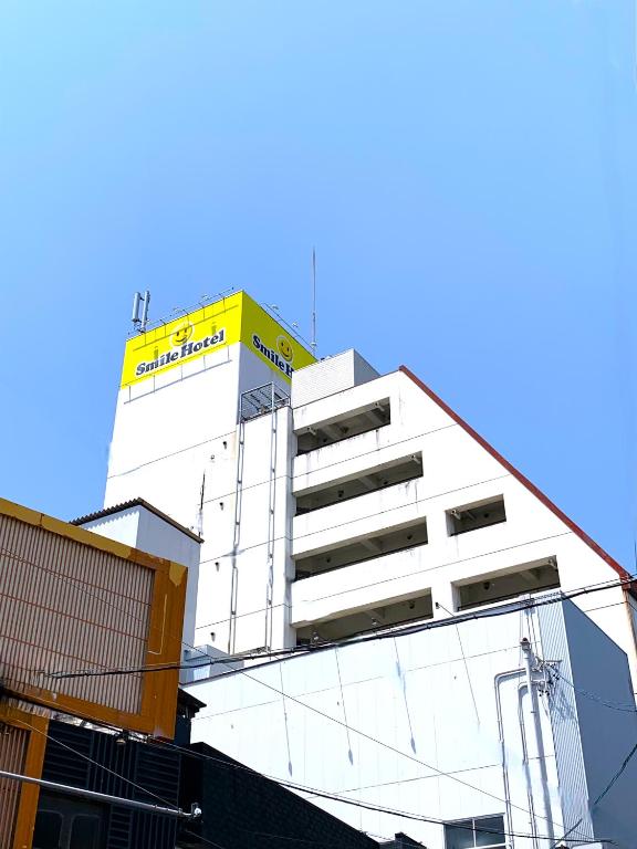 a white building with a yellow sign on top of it at Smile Hotel Nabari in Nabari