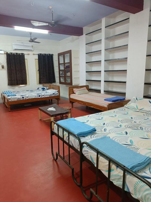 a room with three beds and tables in it at Adb's Kuzhlam Traditional Homestay & Rooms in Tiruchirappalli