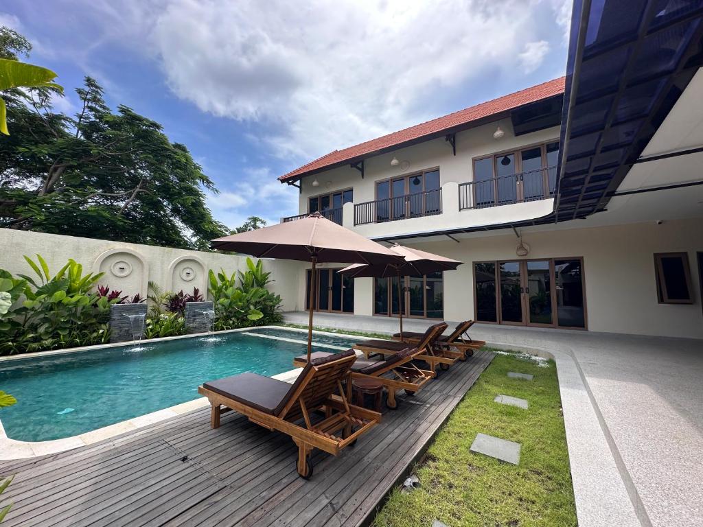 a pool with chairs and an umbrella next to a house at Wanaseta Guesthouse in Uluwatu