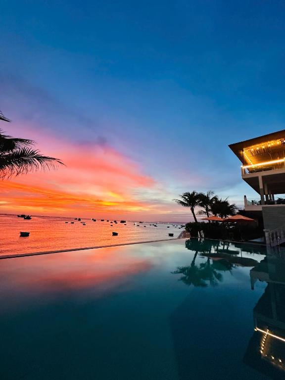 a swimming pool with a view of the ocean at sunset at Bay View Resort & Villas Mũi Né in Phan Thiet