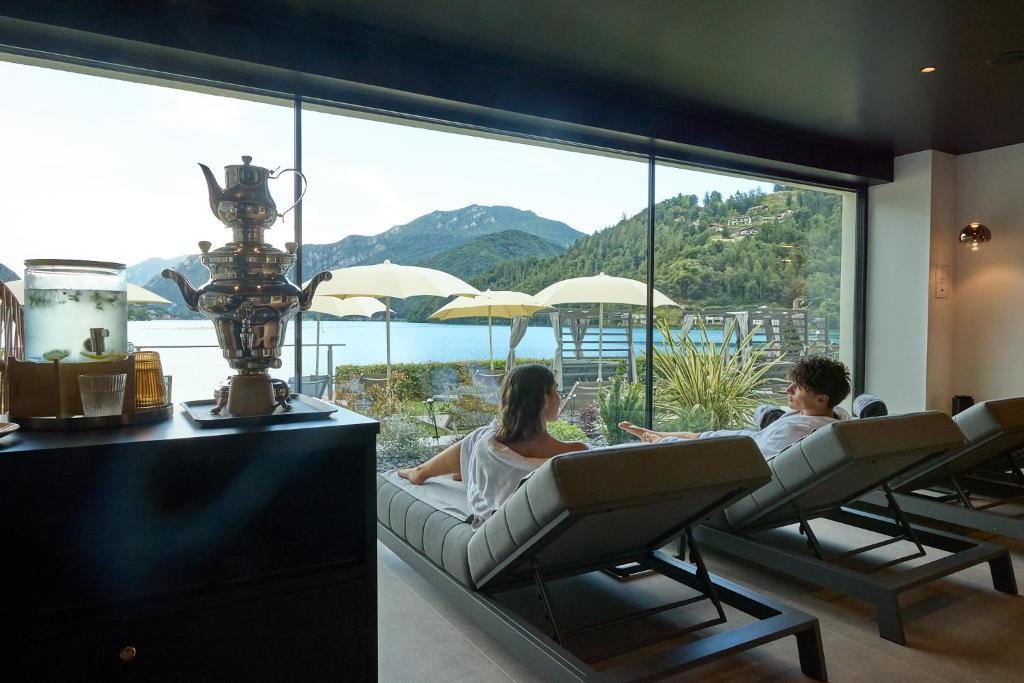 two people sitting in chairs in front of a large window at Hotel Lido in Ledro