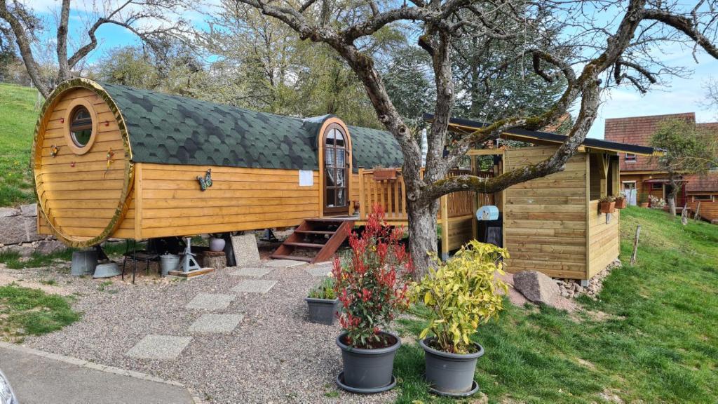 ein großes Holzhaus mit einem Baum und einigen Pflanzen in der Unterkunft Roulotte avec spa privé in Villé
