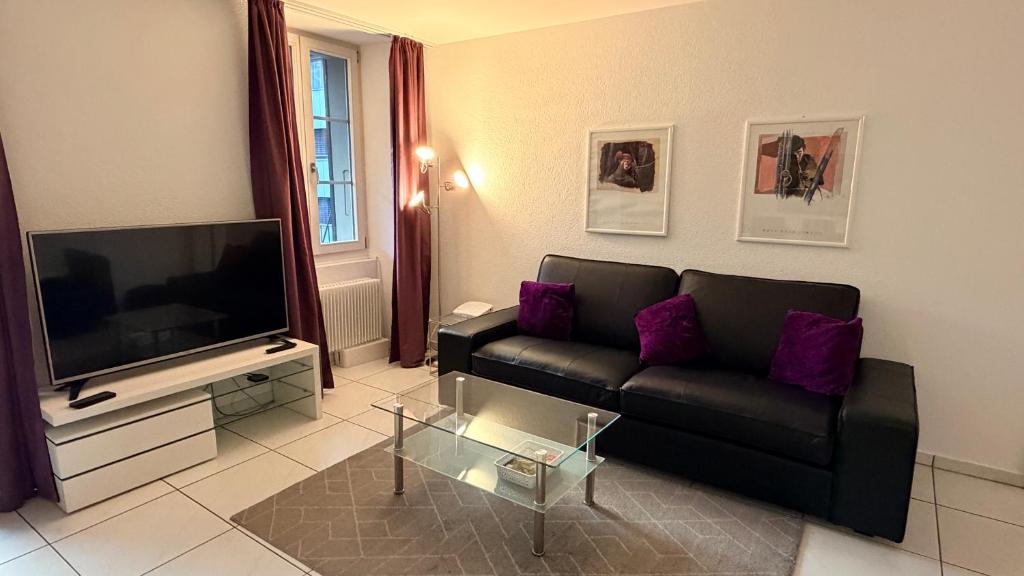 een woonkamer met een zwarte bank en een flatscreen-tv bij Swiss Interlaken Apartment in Interlaken