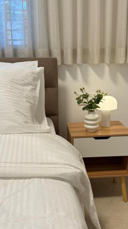 a bed with white sheets and a plant on a night stand at Ramon Palms in Mitzpe Ramon