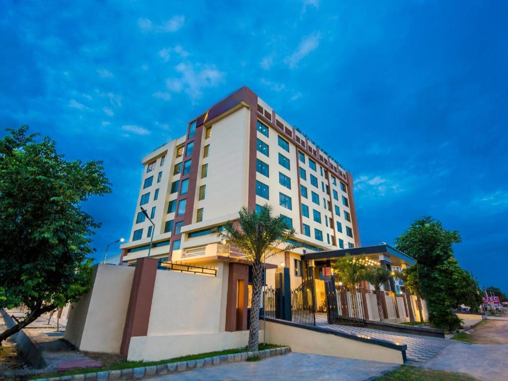 a tall white building with a palm tree in front of it at Golden Tulip Kukas Jaipur in Jaipur