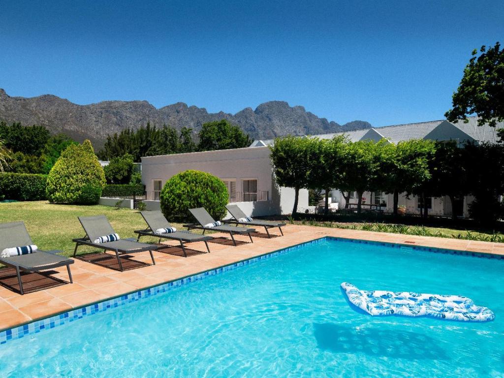 a swimming pool with chairs and a house at La Jolie Dauphine Guest House in Franschhoek