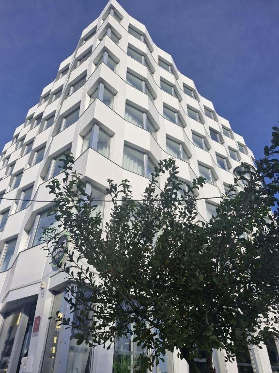 a tall white building with a tree in front of it at B&B HOTEL Massy Gare TGV in Massy