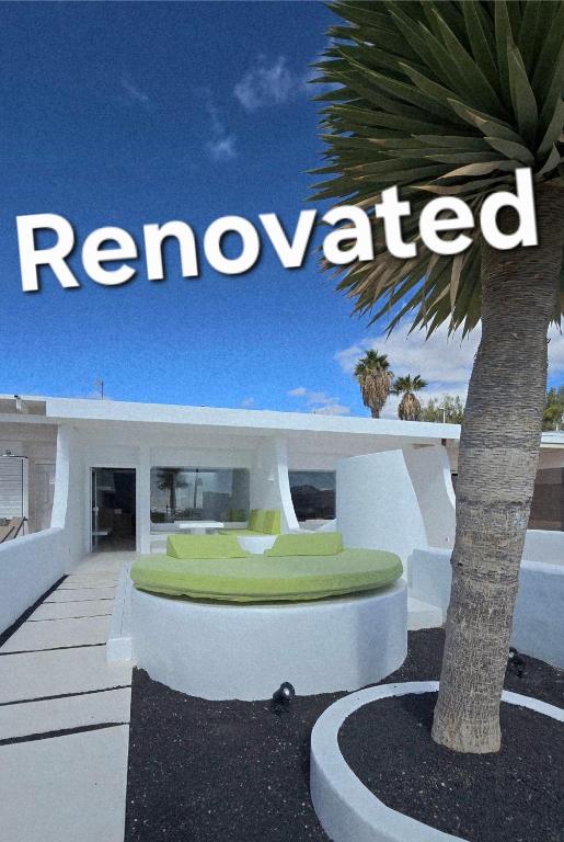 a sign that reads reinvented next to a palm tree at Bungalows Villas Blancas in Puerto del Carmen