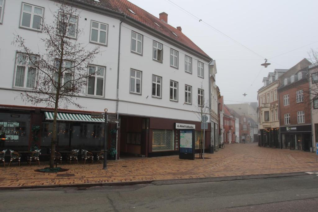 een stadsstraat met een wit gebouw en tafels en stoelen bij The Cozy Cave Odense Center in Odense