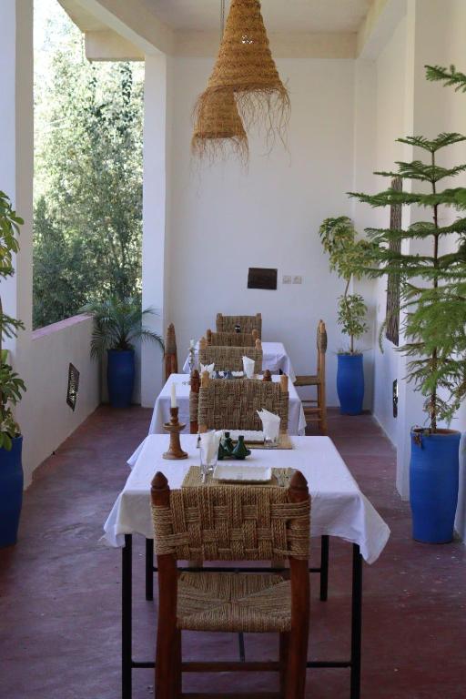 a dining room with tables and chairs and plants at Maison d'Hôte Argana in Aït Idaïr