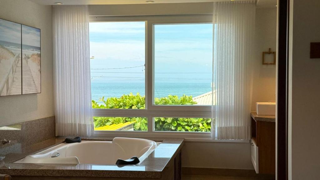 a bathroom with a tub and a large window at Pousada Gamboa estações in Garopaba