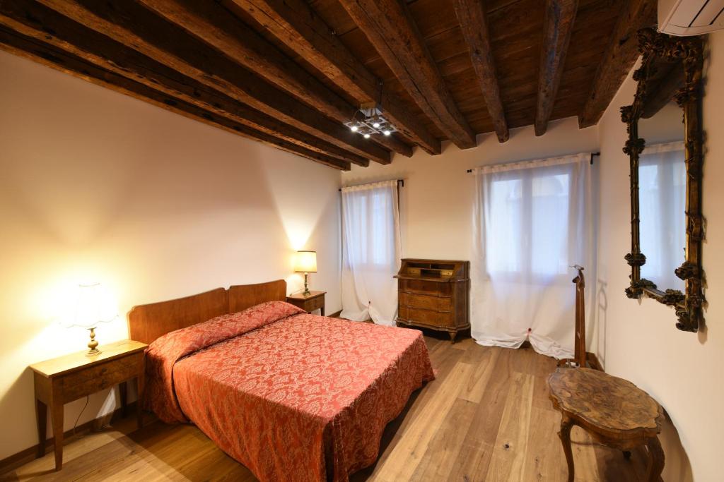 a bedroom with a bed and a table and two windows at Mercerie e Capitello Apartments in Venice