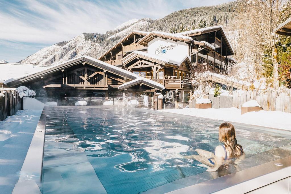 a woman sitting in a hot tub in front of a hotel at Les Gentianettes Hotel & Spa in La Chapelle-dʼAbondance