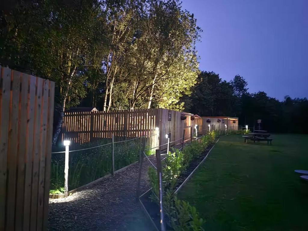 The Forest Pod - Wood Fired Hot Tub and Fire Pit في Hambleton: حديقة مسيجة وبها طاولة نزهة ليلاً