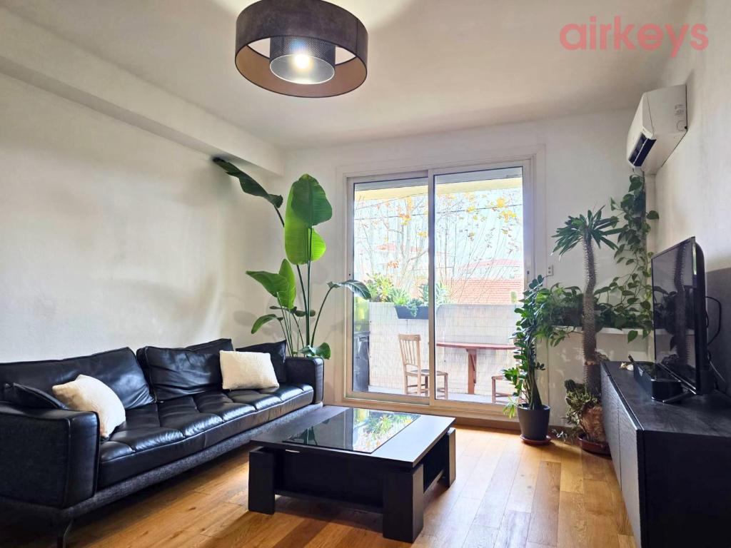 a living room with a black leather couch and a table at Le Fit and Chill - Confort & Calme - Parking - Proche Aéroport et Plage du Jaï in Marignane