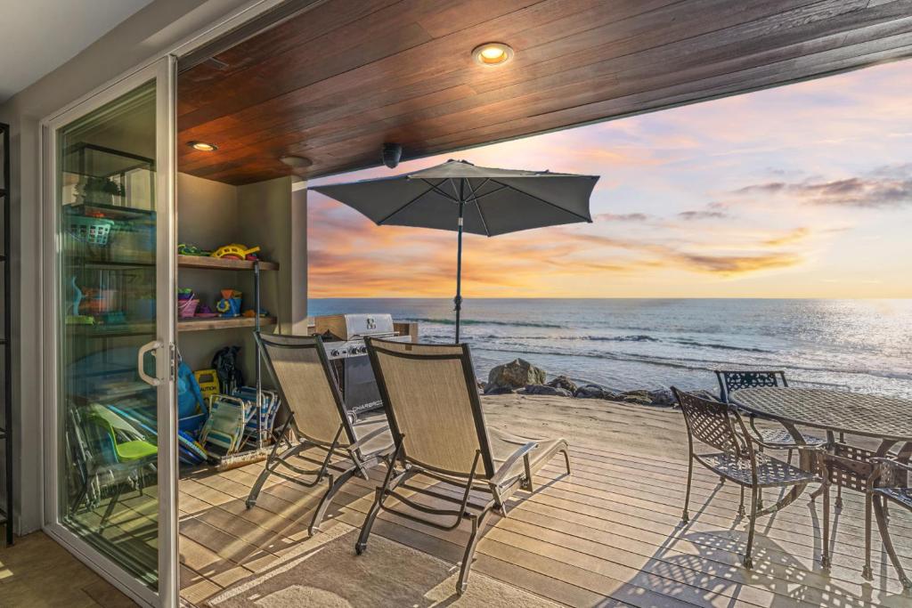 eine Terrasse mit Tisch, Stühlen und Sonnenschirm in der Unterkunft Hawaiian Style Beachfront on Beach Road in Capistrano Beach