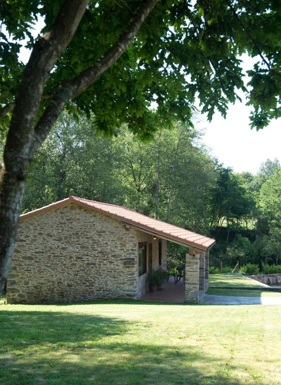 a stone building with a roof on a grass field at A Maquía de Medín in O Pino 