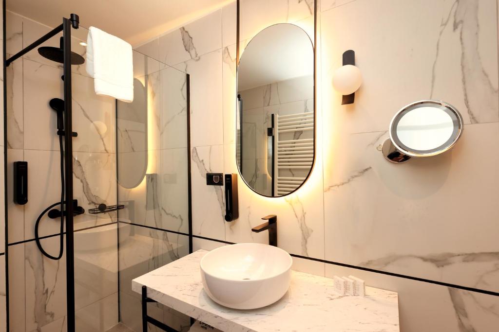 Glass shower with rain head and black wall-mounted faucets, backlit round mirror, heated towel rack and vessel sink at Zeus Essence Bucharest Opera in Bucharest