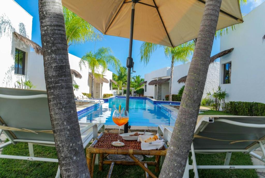 a table with an umbrella next to a swimming pool at Oasis Tajaja Pousada Boutique na Costa do Conde in Jacumã