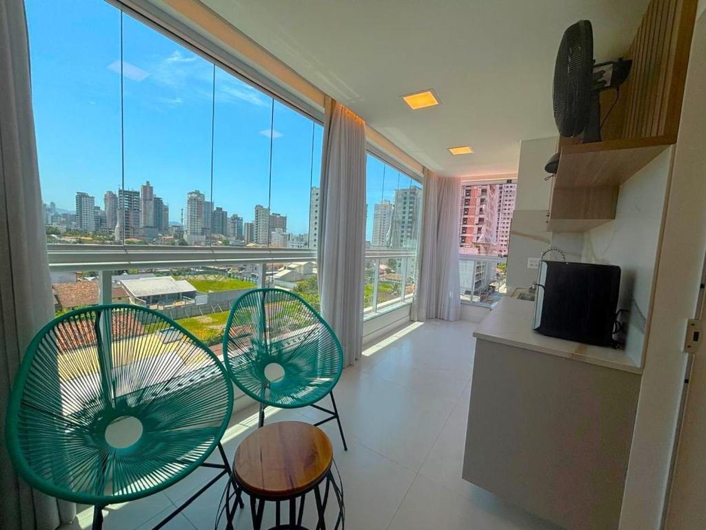 Una cocina con dos sillas verdes y una gran ventana. en Apto c/ parrilla a 450 m del mar, Perequê SRF0601, en Perequê