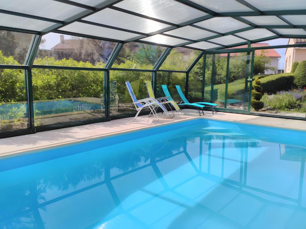 ein Schwimmbad mit einem Glashaus mit Stühlen und einem Schwimmbeckenschirm in der Unterkunft Gîte Le Campet in Millau