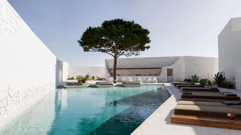 una piscina con sedie e un albero in un edificio di ANOME Mykonos a Ornos