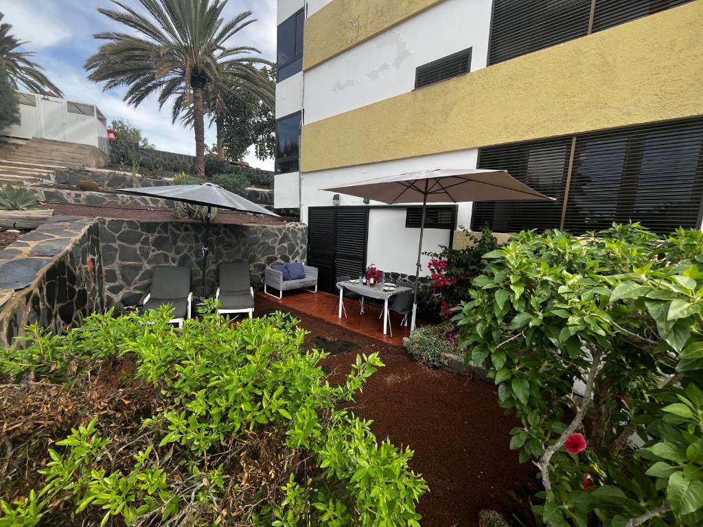 a patio with a table and an umbrella and some bushes at Oasis de paz junto al mar in Maspalomas