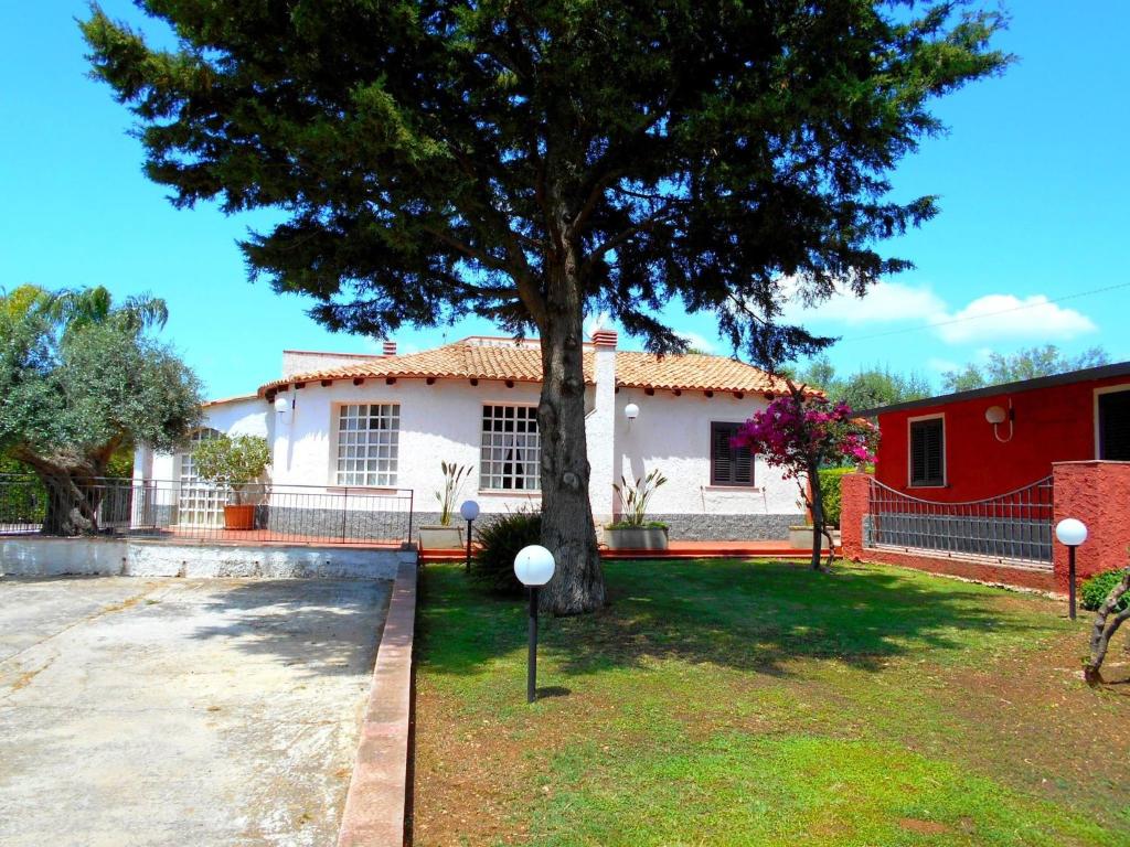 a white house with a tree in the yard at Spacious villa with a large veranda and pool in Floridia