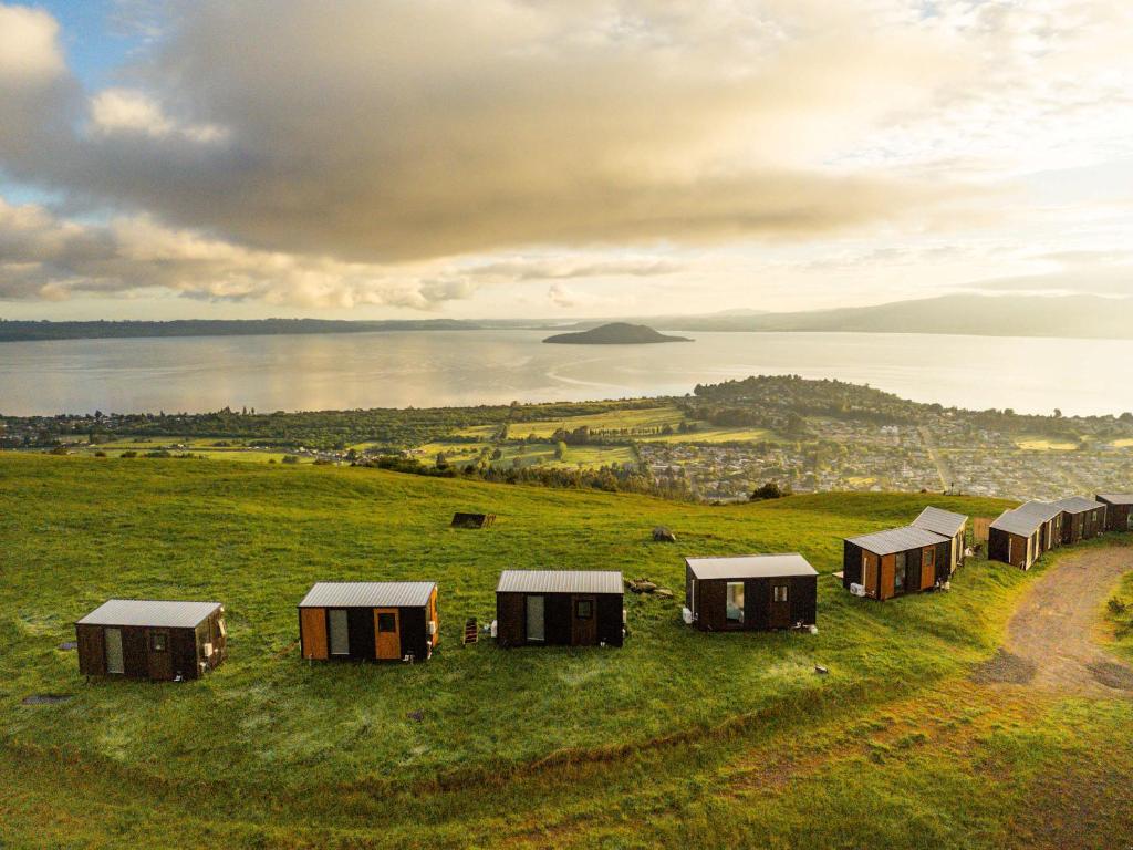 Black Horse Cabin 3 by Tiny Away في Waitoki: مجموعة من الأكواخ في حقل مطل على المحيط
