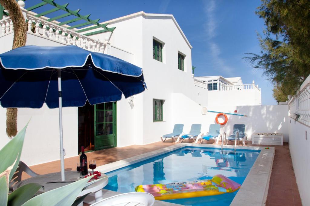 ein Pool mit einem blauen Sonnenschirm und Stühlen in der Unterkunft Villas Bocaina Beach in Puerto del Carmen