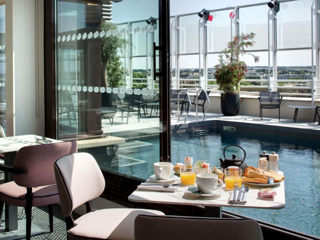 Un restaurante con mesa de desayuno con vista a la piscina. en Pullman La Pléiade Montpellier Centre, en Montpellier