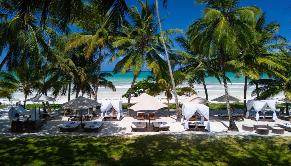 uma praia com cadeiras, guarda-sóis e palmeiras em Almanara Luxury Boutique Hotel and Villas em Praia de Diani