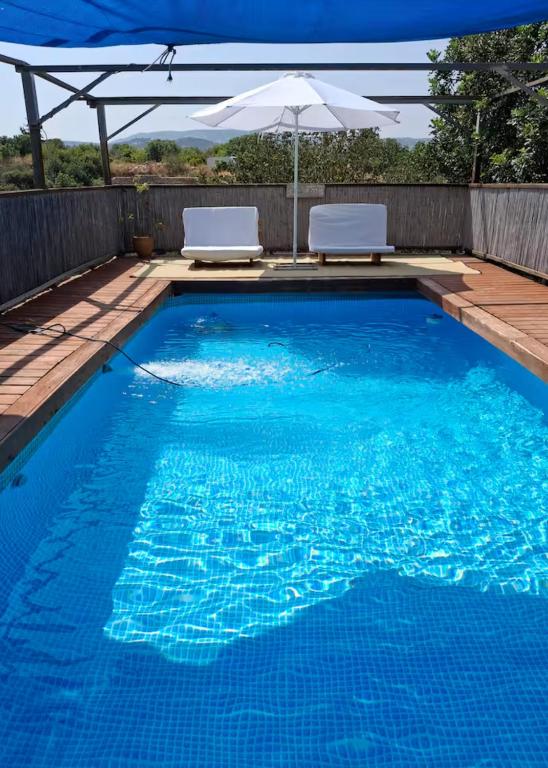 a swimming pool with two chairs and an umbrella at tranquil beautiful house כליל השחר- צימרים קסומים במיקום מרגיע למשפחות וזוגות in Clil