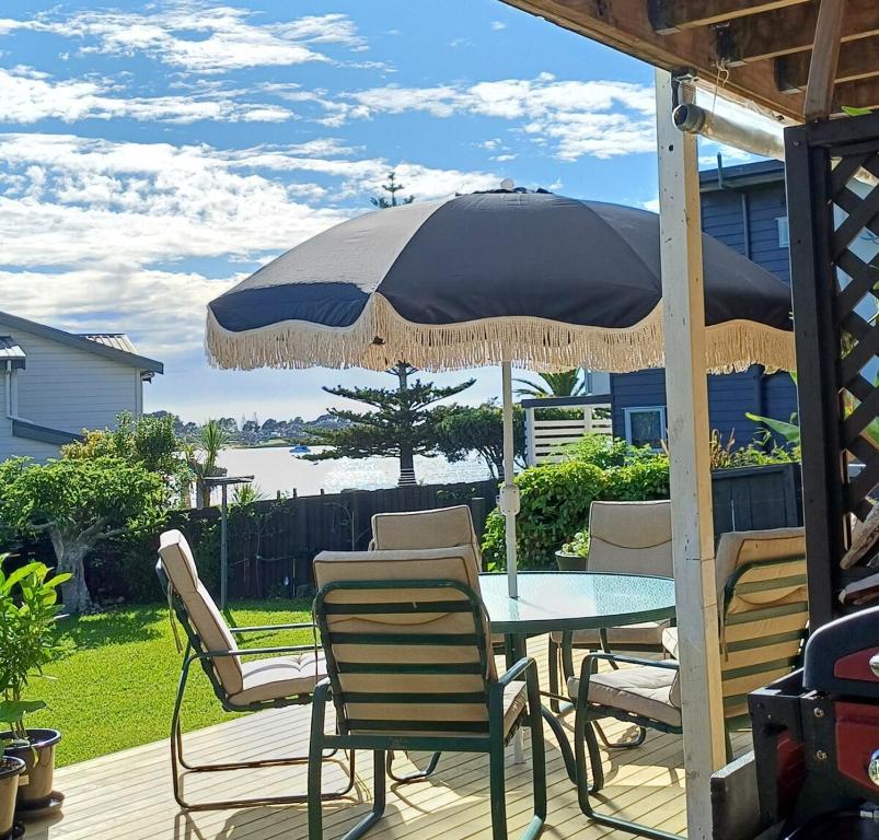a table and chairs under an umbrella on a deck at Driftwood Sands 3 Brm in Tairua
