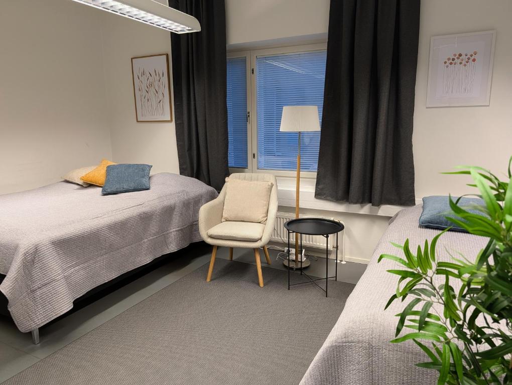 een slaapkamer met twee bedden en een stoel en een raam bij Kotimaailma - Vihtyisä Hostelli in Kokkola