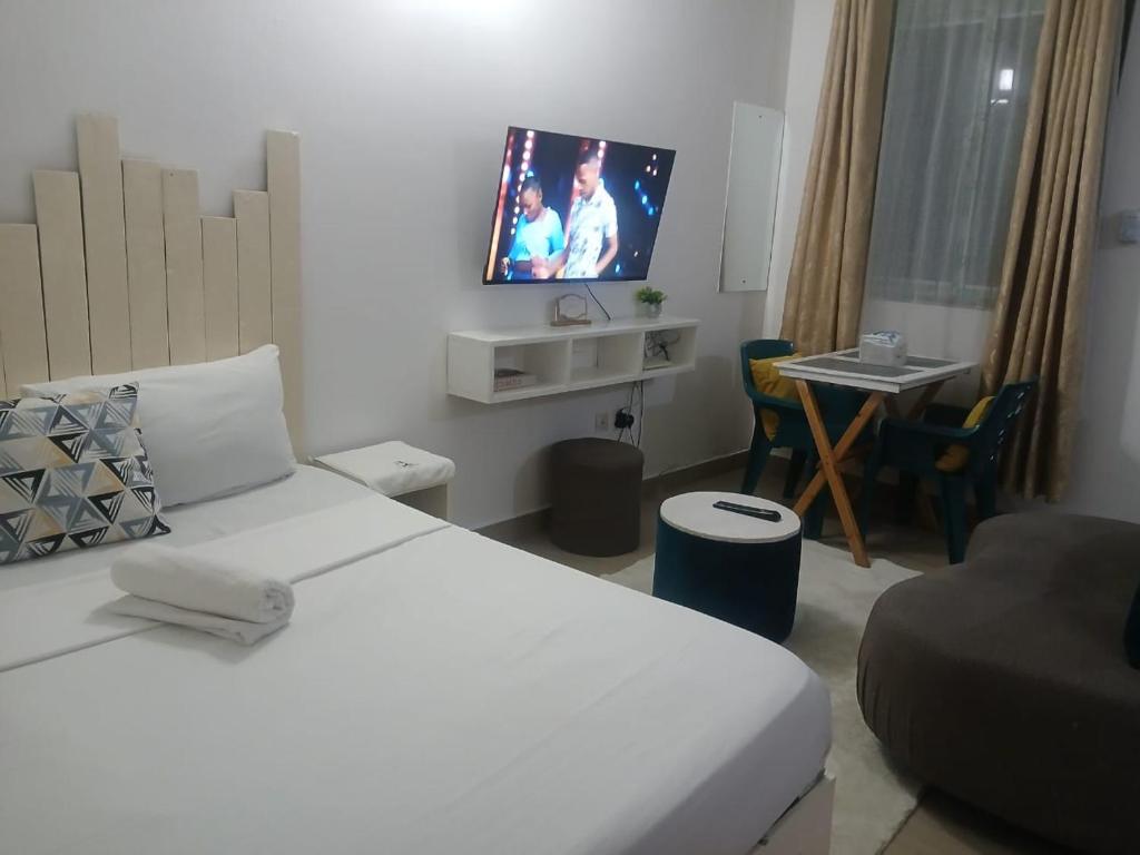 Mash Studio Apartment in Bamburi في مومباسا: غرفة نوم بسرير ابيض وتلفزيون على الحائط
