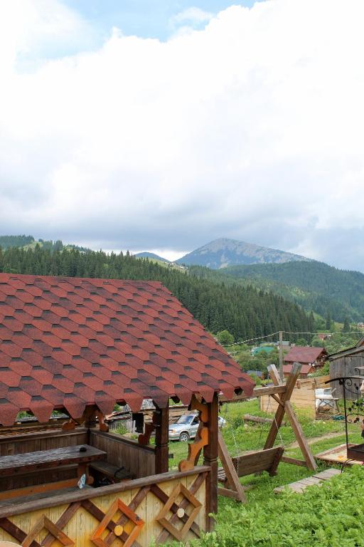 a house with a red roof with mountains in the background at Сільська садиба in Yablunytsya