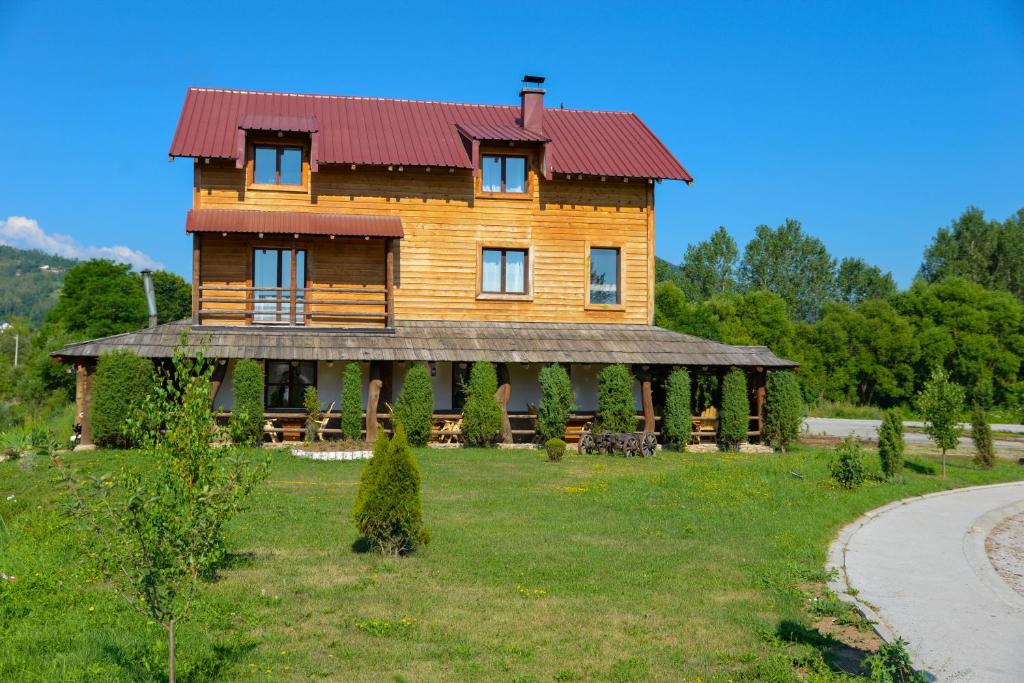 a wooden house with a red roof on a green field at Motel Nacionalni Restoran Ognjiste in Koruge