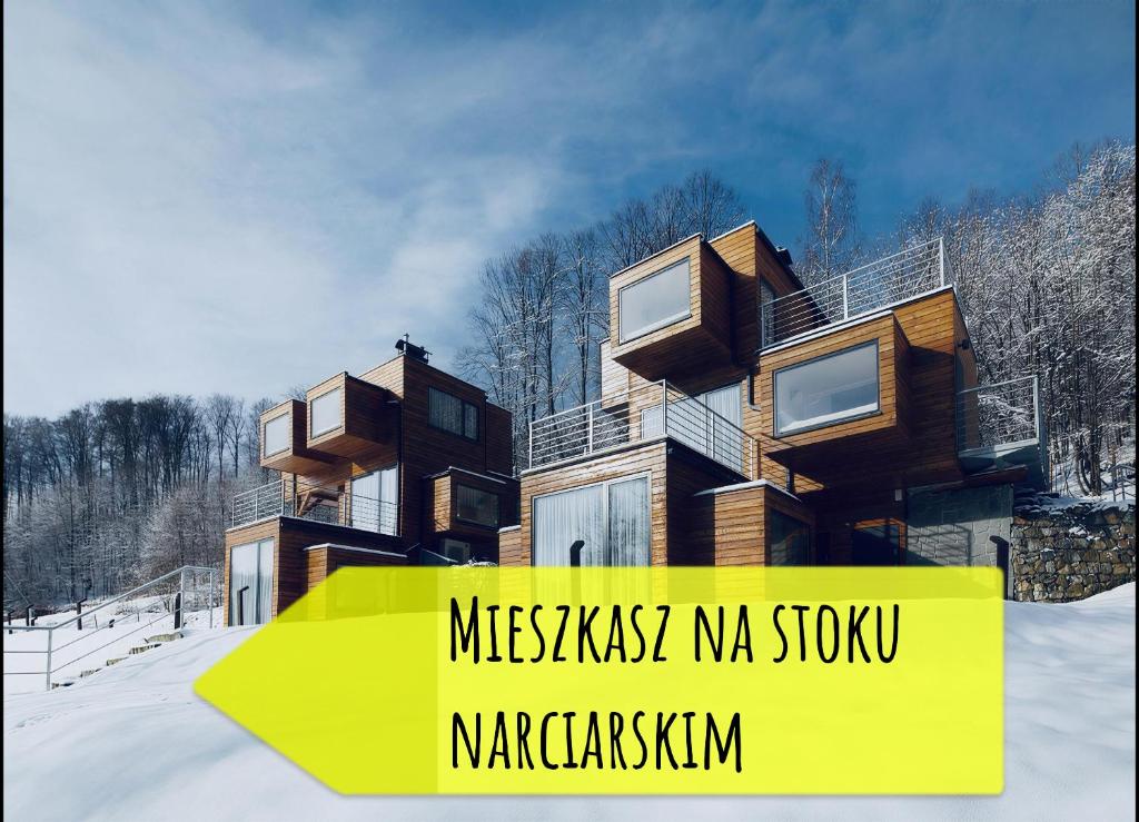Two wooden cube cabins on snowy slope with large yellow promotional banner in the foreground.