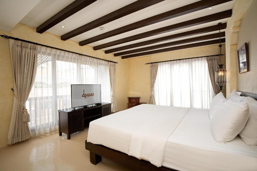 A large bedroom with a white bed, two curtained window areas and a television.