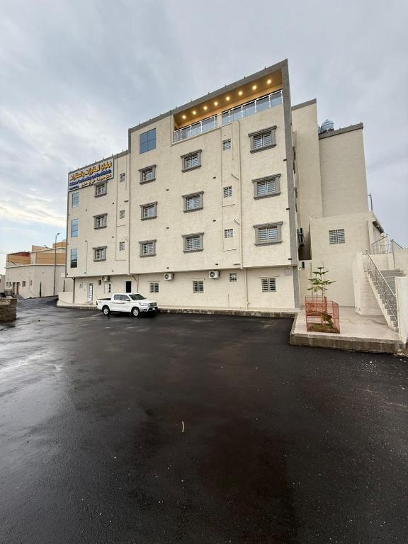 ein großes Gebäude mit einem auf einem Parkplatz geparkten Auto in der Unterkunft شقق نطوان المفروشة in Abha