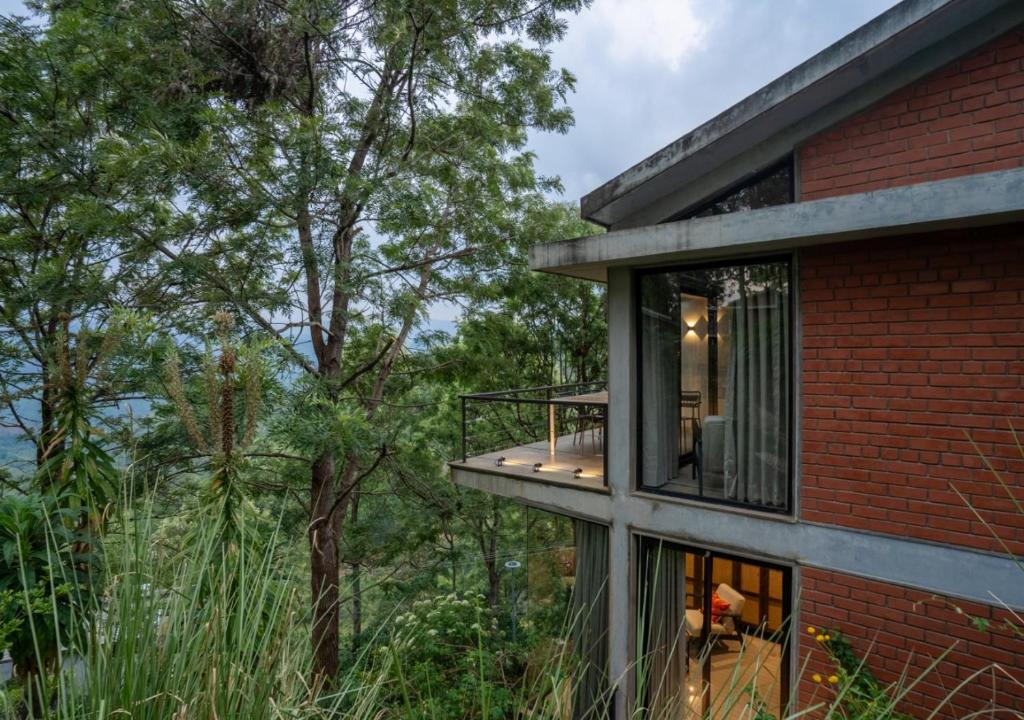 ein Backsteinhaus mit einem Balkon und Bäumen in der Unterkunft LohonoStays Villa Amani 8B in Coonoor